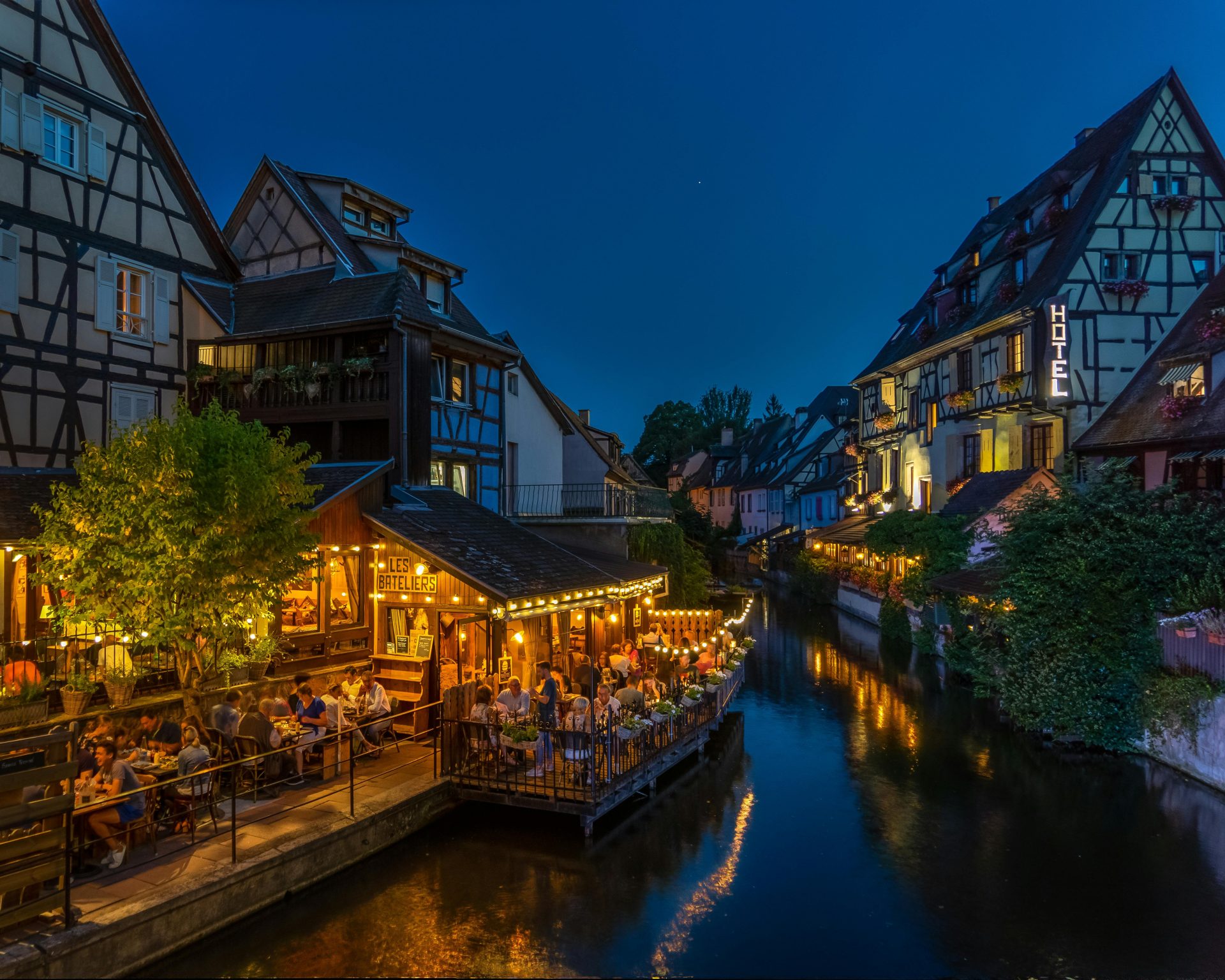 Nighttime view of Colmar's timbered houses and canal-side dining, beautifully illuminated.